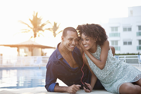 游泳池边分享耳机的时尚夫妇图片