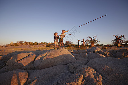 两名男孩站在石头上扔长矛图片