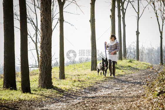 年轻女子和狗狗走在泥土路上图片