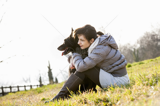 年轻女子和狗狗坐在山坡上图片