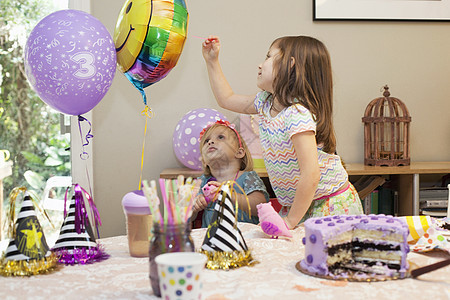 两个女孩坐在生日派对桌边蛋糕玩气球图片