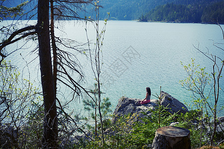 坐在湖边岩石上练习瑜伽的女性图片