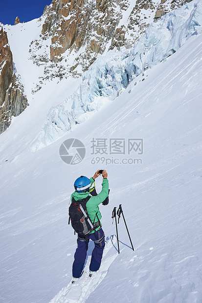 在法国雪山上使用手机拍照的滑雪男子图片