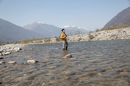 年轻男远足者在河流浅滩中行走背景图片