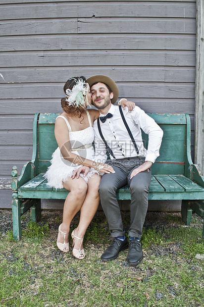 新娘和郎坐在长凳上的肖像新娘在脸颊上亲吻新郎图片