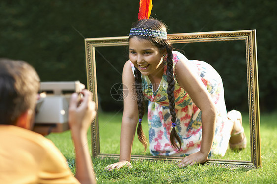 女孩跪着透过相框看正在拍照图片
