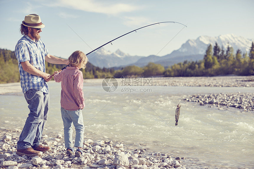 德国巴伐利亚州瓦尔高一对中年男子和一对男孩拿着鱼竿在河边钓鱼图片