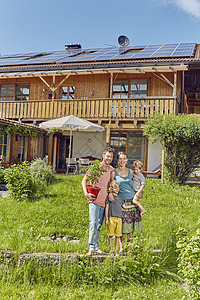 年轻家庭的肖像拿着工厂站在房屋前用太阳能板顶的房屋前图片