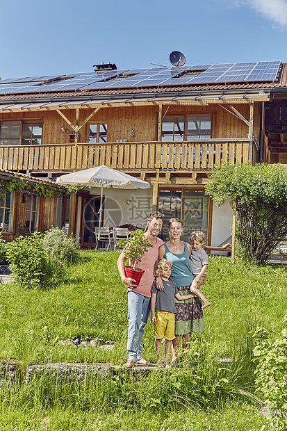 年轻家庭的肖像拿着工厂站在房屋前用太阳能板顶的房屋前图片