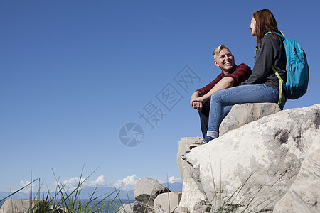 坐在岩石上微笑的年轻夫妇低角度视图片