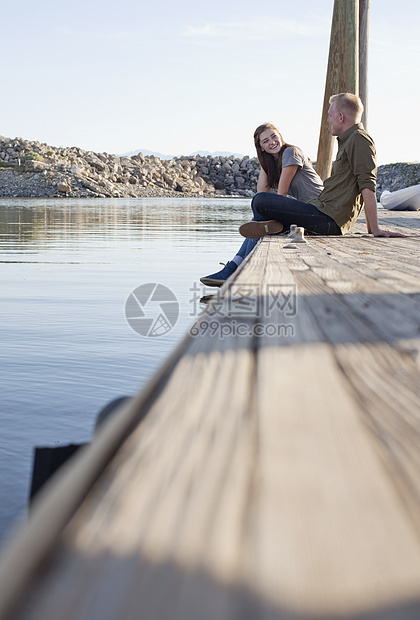 一对年轻夫妇坐在木制码头上聊天的侧视图图片