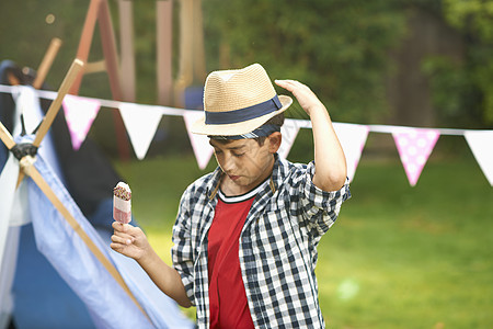 男孩一边在花园里调整帽子一边吃冰棒图片