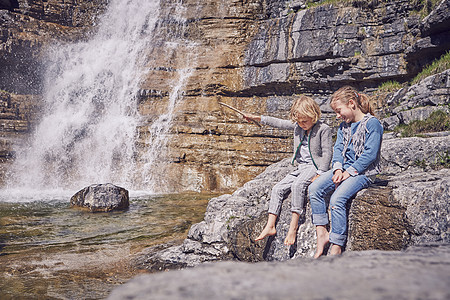 兄妹坐在岩石上放松瀑布旁边图片