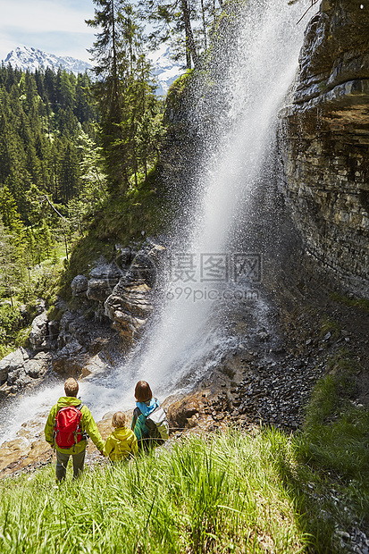 年轻家庭在森林中站立看着瀑后视图片