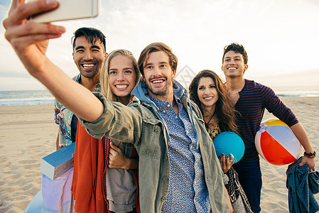 一群朋友在沙滩上用智能手机自拍图片