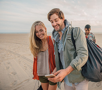一群朋友在海滩上散步一对年轻夫妇看着智能手机图片