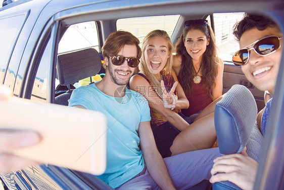 一群坐在车里的朋友带着智能手机拍自肖像笑着图片