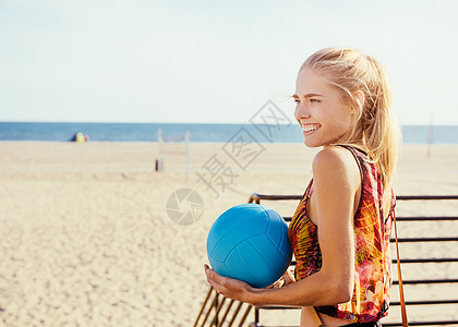 年轻女子站在沙滩旁握着球图片