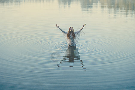 年轻女子站在湖边的波纹中双臂张开图片