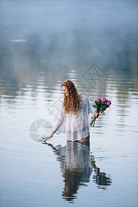 站在湖边的年轻女人拿着一堆玫瑰她的手指撕开地表图片