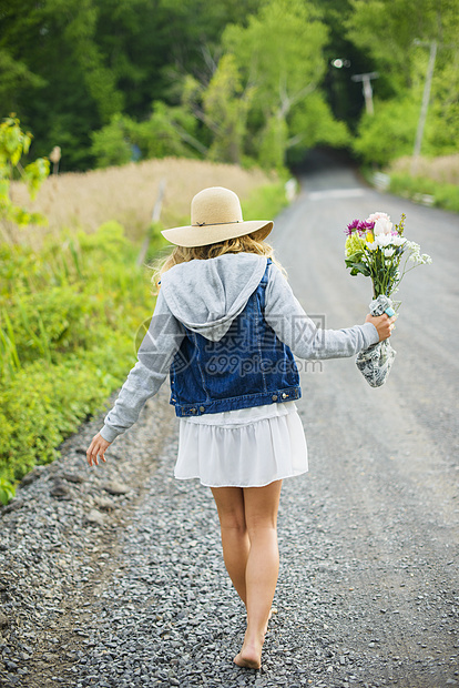 看见赤脚的年轻妇女走在农村砂砾路带着一束鲜花图片