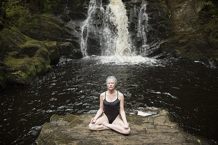在瀑布前做瑜伽的成熟女性图片