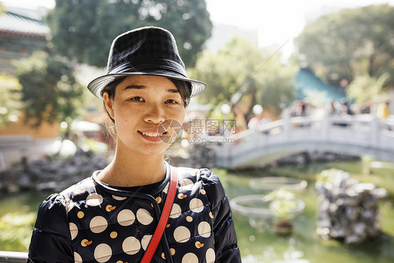 在花园桥前戴帽子的年轻女肖像图片