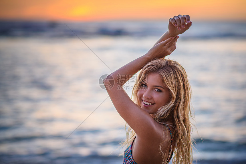 日落时在海滩上举起手臂的年轻女子图片
