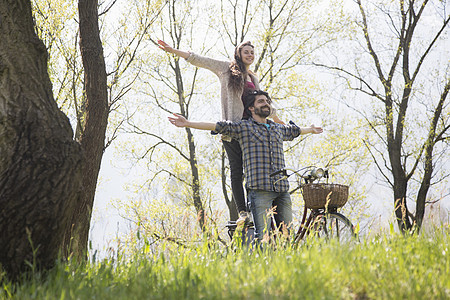 年轻夫妇骑自行车在农村林地张开双臂图片