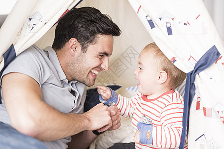 父亲和小儿子坐在室内的游戏帐篷里一起笑着图片
