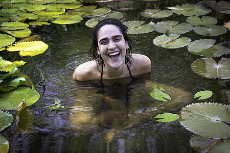 坐在池塘里被荷花环绕着的年轻女子看着镜头微笑图片
