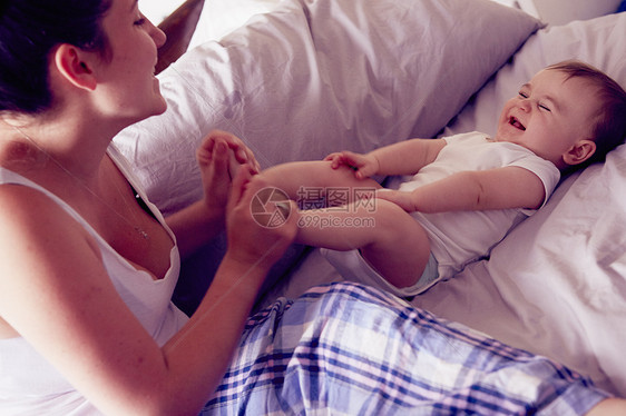 母亲和婴儿男孩在床上玩图片