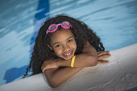 长着卷发黑女孩的肖像挂在游泳池的边缘看着镜头微笑图片