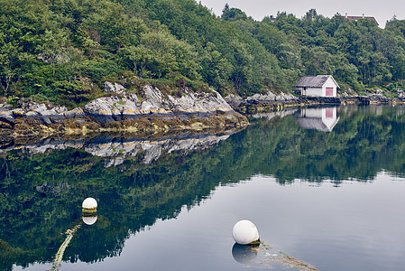 挪威罗加兰县豪格松平静水中的船库和树木倒影图片
