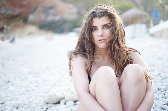 西班牙贾韦亚海滩上抱着膝盖的长棕色头发少女图片