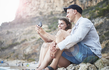 在西班牙哈韦亚的岩石海滩阅读智能手机短信图片