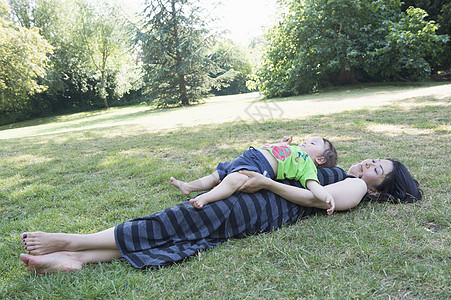 母亲抱着儿子躺在草在公园地上图片