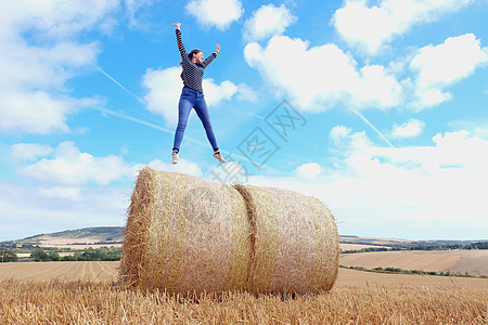 年轻妇女在收获田干草堆上跳跃图片