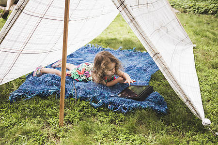 女孩躺在花园帐篷里玩平板电脑图片