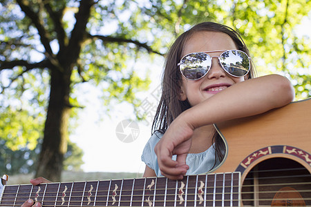 小女孩带着墨镜在公园撑着吉他微笑图片