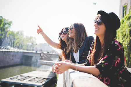 三个时尚的年轻女朋友在城市河边仰望图片
