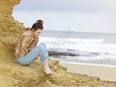 年轻女子裹着披肩坐在悬崖边图片