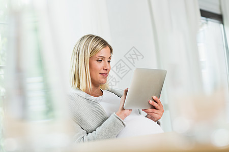 在数字平板电脑上使用触摸屏的足月怀孕年轻女人图片