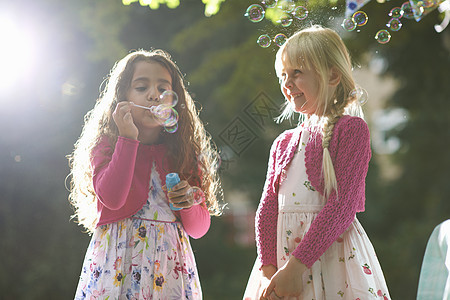 两个可爱的女孩在阳光花园吹泡泡图片