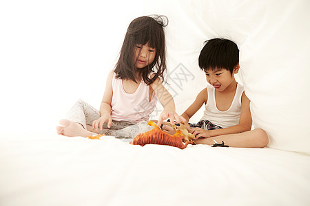 年轻的男孩和女孩在床上玩着床单下的玩具图片