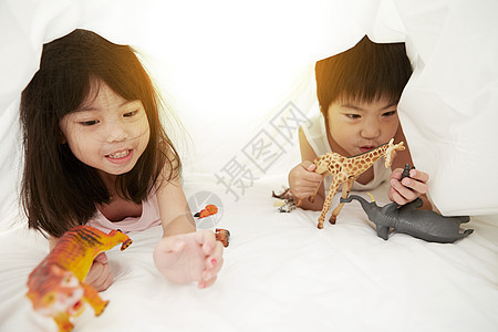 年轻的男孩和女孩在床上玩着床单下的玩具图片