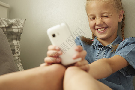 女孩坐在靠墙着拿智能手机闭上眼睛笑着图片