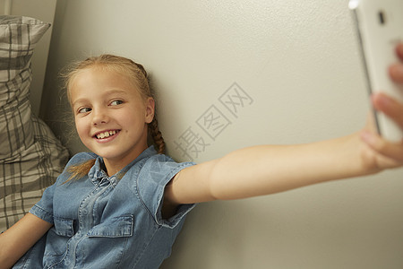 女孩靠在墙上使用智能手机取笑自拍图片