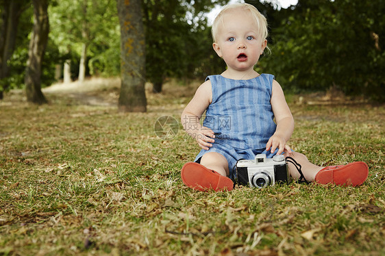 婴儿女孩坐在草地上用胶片摄影机坐在草地上看着照相机张嘴图片