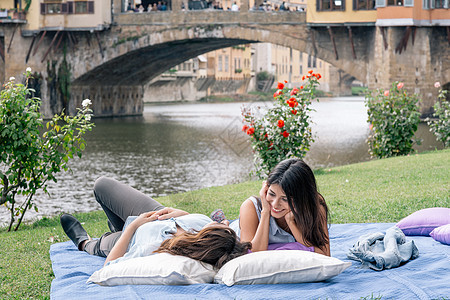 在意大利托斯卡纳州佛罗伦萨河的面前躺在毯子上的一对少女图片